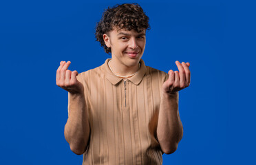 Smiling man asking money gesture on blue studio background. Smart curly dude