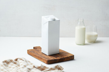 White Carton of Milk on Wooden Cutting Board With Glass and Bottle of Milk in Background