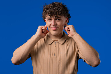 Annoyed man with shut ears on blue. Guy block annoying sounds, loud music, noise