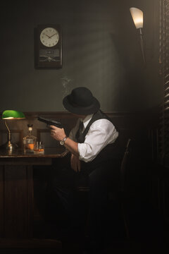Portrait of  detective is sitting behind the table and playing with the gun in his vintage office