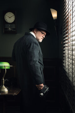 Portrait of the man in grey trench and film camera near the window in vintage detective office