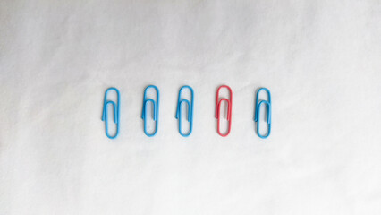 Five paper clips, red among the blue, arranged in a line against a white surface. Concept of uniqueness, outlier, be different, or embrace diversity.