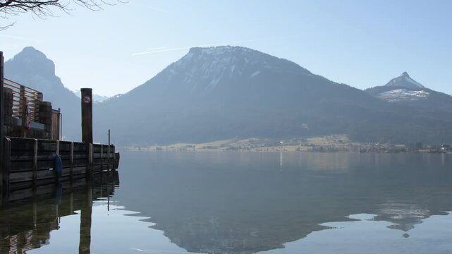 Mirroring the mountains in the water - the clear morning sky, snow-capped peaks and the smooth surface of the lake create a picturesque landscape, St Wolfgang, Austria.