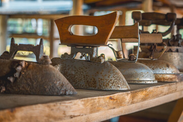 several old antique vintage irons on a shelf in a shed in the countryside