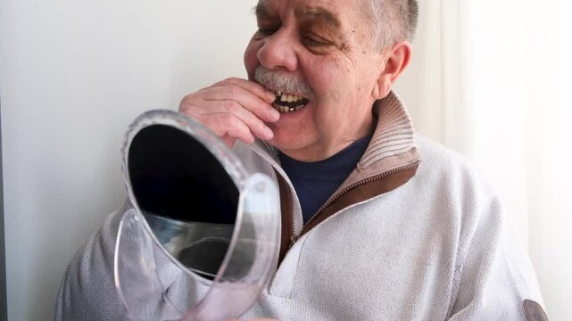 An elderly man holds a denture in his hands. The concept of stomatology and prosthetics. A dental prosthesis. Dentures on hooks