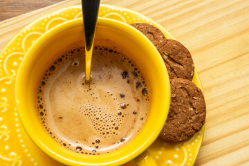 Close up em uma xícara amarela com cappuccino cremoso e alguns cookies no píres sobre superfície...