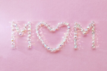 Stylish Mother's Day card, text "Mom" made of transparent iridescent beads on a textured pink background. Mother's Day celebration concept
