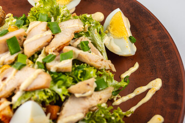 Delicious Caesar salad with grilled chicken, boiled eggs, fresh lettuce, corn and creamy dressing on a brown clay plate. A healthy and tasty dish for a perfect lunch