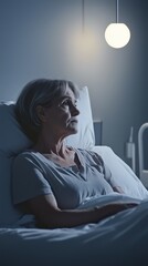 Fototapeta premium A mature woman lies in bed, illuminated by soft light, appearing contemplative and serene in a tranquil setting.