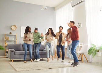 Optimistic carefree women and men friends having fun together in modern apartment, dancing to music as having home party, celebrating something together, being in good mood. Friendship concept