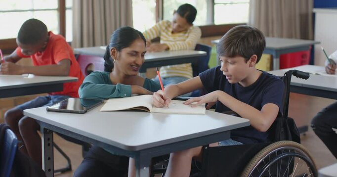 In school, teacher assisting student in wheelchair with writing in classroom