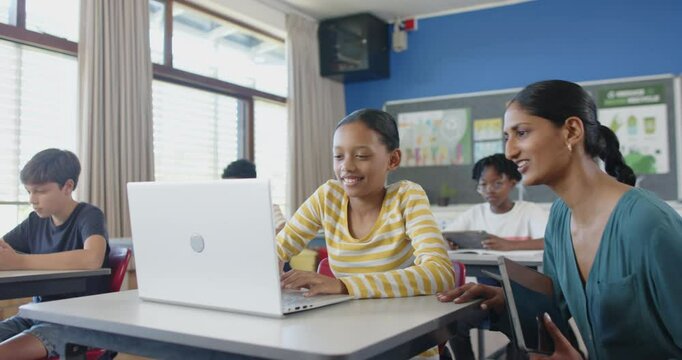 Helping student using laptop in classroom, teacher collaborating on school project
