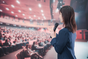 大勢の聴衆が集まるホールで司会をする若い女性