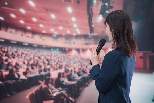 大勢の聴衆が集まるホールで司会をする若い女性