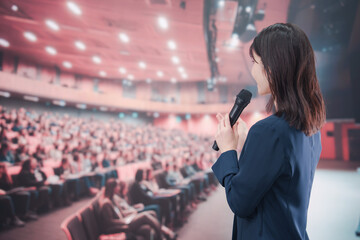大勢の聴衆が集まるホールで司会をする若い女性