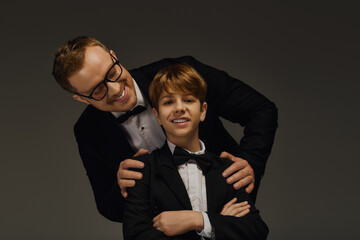 Handsome father and son share a joyful moment in elegant tuxedos in a studio setting