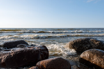 Foaming sea waves roll frontally and rhythmically onto large pink granite stones. Blue sky on a...