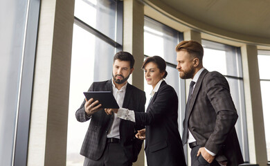 Business people group of three standing in modern office hall near window, supervisor with team, workers, office employees discussing project, sharing ideas, brainstorming, businesspeople gather