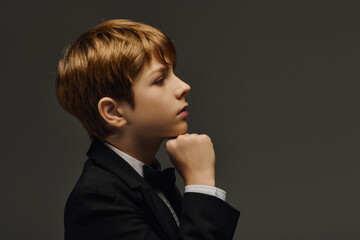 Elegant preteen boy in bow tie poses thoughtfully in stylish studio setting