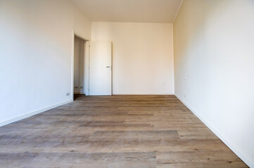 Empty room with wooden floor and white walls featuring a open door