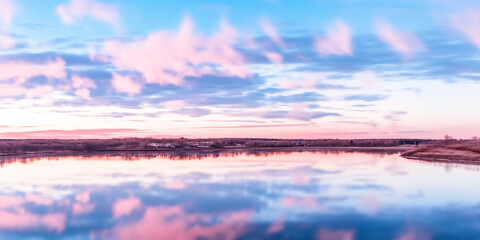 A serene lakeside view reflecting colorful clouds at sunset.