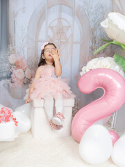 Generated A little girl in pink clothing celebrates in a fairy-tale setting with pastel decorations, a large pink balloon in the shape of a two, and white flowers, radiating joy and innocence.