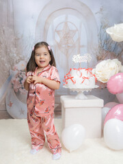 Generated A little girl in pink clothing celebrates in a fairy-tale setting with pastel decorations, a large pink balloon in the shape of a two, and white flowers, radiating joy and innocence.