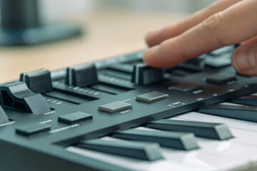 Woman playing MIDI keyboard with control knobs and pads, close-up.