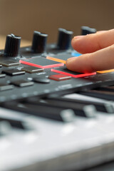 Woman playing MIDI keyboard with control knobs and pads, close-up.