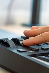 Woman playing MIDI keyboard with control knobs and pads, close-up.