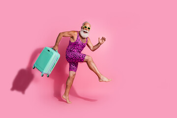 Photo of positive optimistic man wear swimsuit hold valise hurry airport departure vacation isolated on pink color background