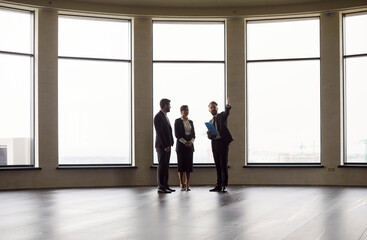 Professional man realtor agent showing empty modern office space for a rent to a young cheerful business people wearing formal clothes going to make a deal. Real estate market concept.