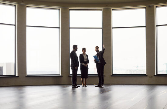 Professional man realtor agent showing empty modern office space for a rent to a young cheerful business people wearing formal clothes going to make a deal. Real estate market concept.