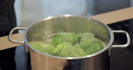Broccoli florets are gently placed into a pot of boiling water for cooking, the hot steam rises as the vibrant green vegetable begins to blanch in the bubbling liquid
