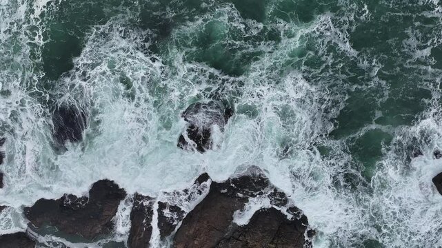 Aerial slow-motion showcasing the foamy waves from above, crashing a rocky shore
