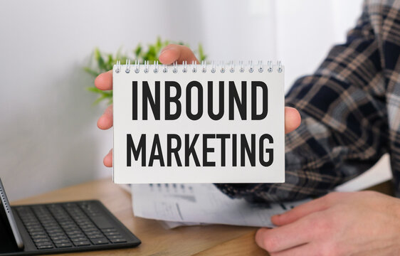 A person is holding a spiral bound notebook with the word Inbound Marketing