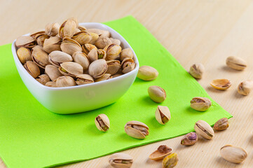 Pistachios in shell, in white bowl, on green napkin and wooden surface. Properties and uses of pistachio.