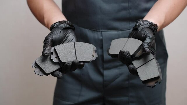 Auto mechanic holds brake pads of car in hands in black gloves, close-up. Concept auto parts replacement, car maintenance, brake system serviceability