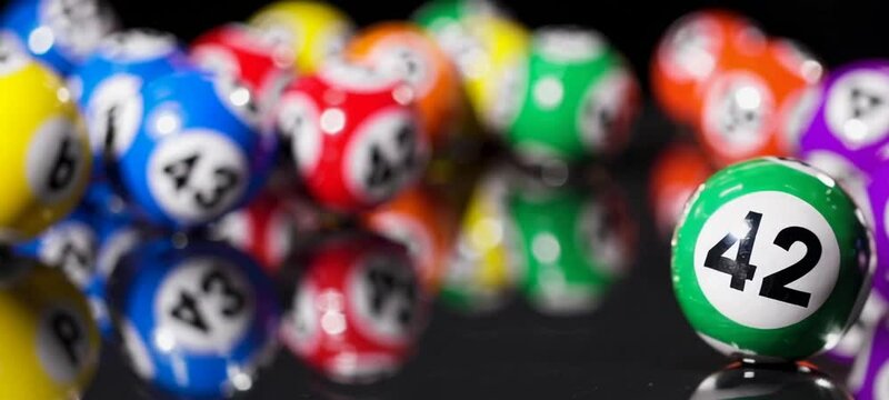 Multicolored bingo balls in focus amidst a blur of vibrant movement on reflective surface