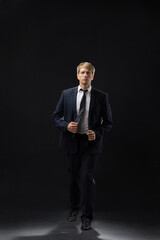 confident man strides forward in a dark suit, exuding authority and professionalism. The low-key,...