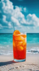 Refreshing orange cocktail on a sandy beach with turquoise ocean and cloudy sky in the background evoking summer vacation