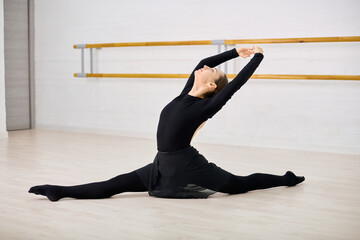 Young ballerina in black leotard performs split in dance studio