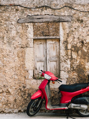 Red scooter in front of weathered wall. Red scooter parked near old weathered stone wall with wooden window in typical Greek village, contrast between old and new. relaxed Mediterranean lifestyle © Viktar Vysotski