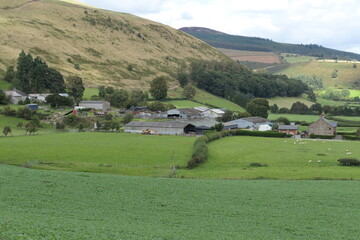 A classic Welsh agricultural landscape with rolling green hills, a small farm, and a wide rural view stretching into the distance.