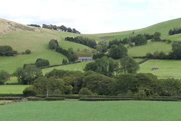 A classic Welsh agricultural landscape with rolling green hills, a small farm, and a wide rural view stretching into the distance.