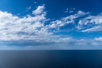 A tranquil blue ocean meets a serene sky adorned with soft, fluffy clouds on a sunny day.