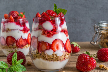 Strawberry yogurt parfait with granola and fresh mint in glasses on rustic wooden table with whole...