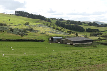 A classic Welsh agricultural landscape with rolling green hills, a small farm, and a wide rural view stretching into the distance.