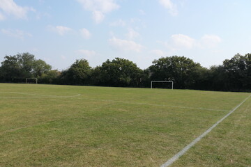 A soccer goal on a green field, framed by a tree-lined edge in the background.