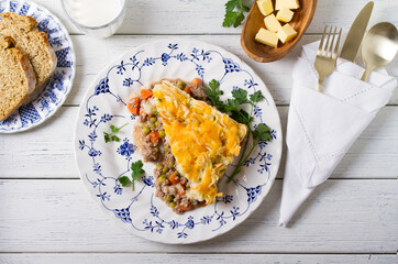 Shepherd's Pie or Cottage Pie on white plate. Savory pie made with beef mince and vegetables topped with mashed potatoes and cheese. View from above, top view